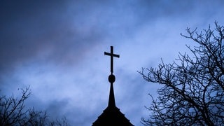 Ein Kreuz vor dunklen Wolken - ein Priester aus dem Westerwaldkreis ist wegen des Verdachts auf Kindesmissbrauchs angeklagt worden.