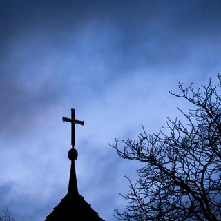 Ein Kreuz vor dunklen Wolken - ein Priester aus dem Westerwaldkreis ist wegen des Verdachts auf Kindesmissbrauchs angeklagt worden.