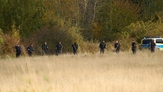 Polizisten durchkämmen mit Stöcken das Gebiet um den Fundort von zwei Männerleichen am Rodder Maar