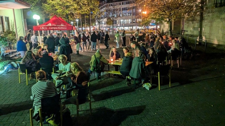 Mehrere Menschen sitzen an Bierzelt-Tischen an der Herz-Jesu-Kirche in Koblenz und essen das Essen der 