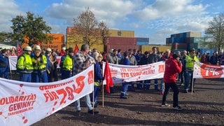 Warnstreik der IG Metall bei Novelis in Koblenz: Mitarbeitende stehen mit Transparenten vor dem Firmengelände