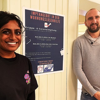 Zwei Menschen stehen vor einer Wand neben einem Plakat. Anna Lena Gerz und Andreas Wilting organsieren das Impfprojekt für Wohnungslose in Koblenz. 