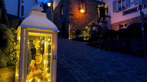 Eine Laterne mit Krippe leuchtet im Dunkeln im Jahr 2023 am Krippenweg in Monreal.