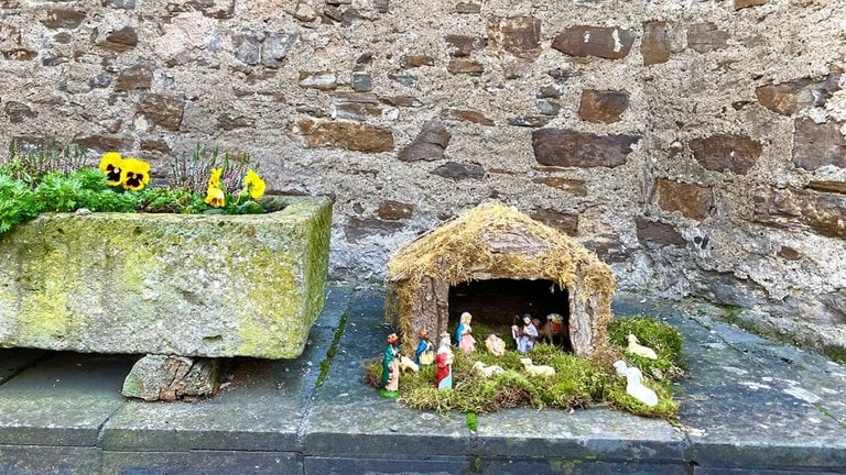 Eine kleine Krippe steht vor einer Bruchsteinmauer am Wichtelweg in Monreal: Ein schönes Ausflugsziel im Advent und der Weihnachtszeit 2024 mit Kindern. 