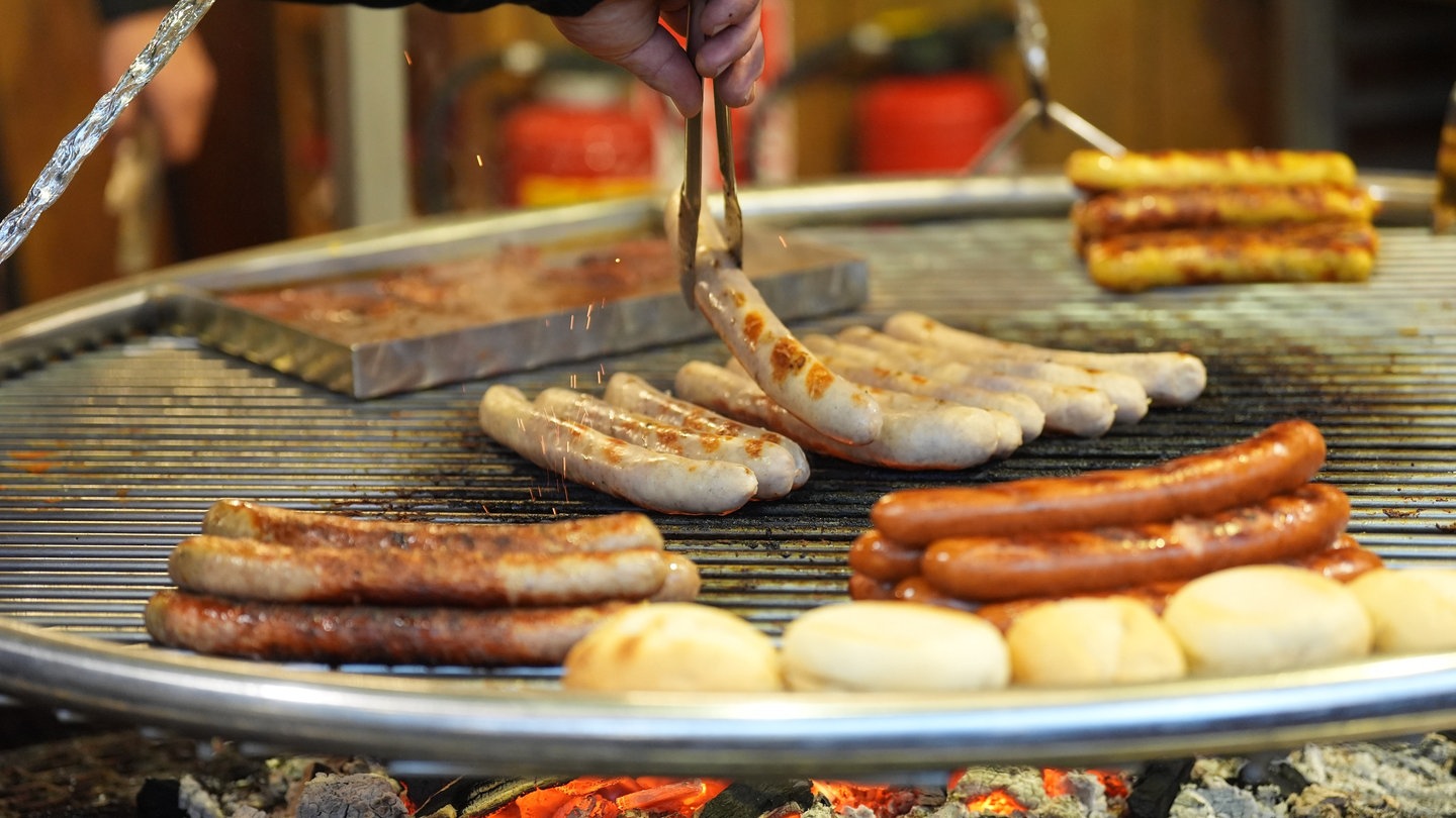 Viele Bratwürste werden auf großem Rost gegrillt.