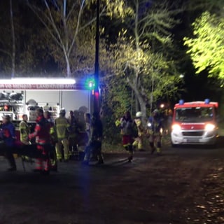 Einsatzkräfte der Feuerwehr und Bergwacht stehen in der Nähe des Unglücksortes in Mendig. Dort waren am Sonntagabend drei Jugendliche in einen rund zehn Meter tiefen Schacht gestürzt. Sie wurden schwer verletzt von der Bergwacht geborgen und in Krankenhäuser gebracht.