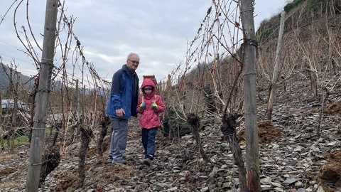 Ein Mädchen trägt einen Korb auf dem Rücken. Neben ihr steht ein älterer Mann im Weinberg in Lehmen.