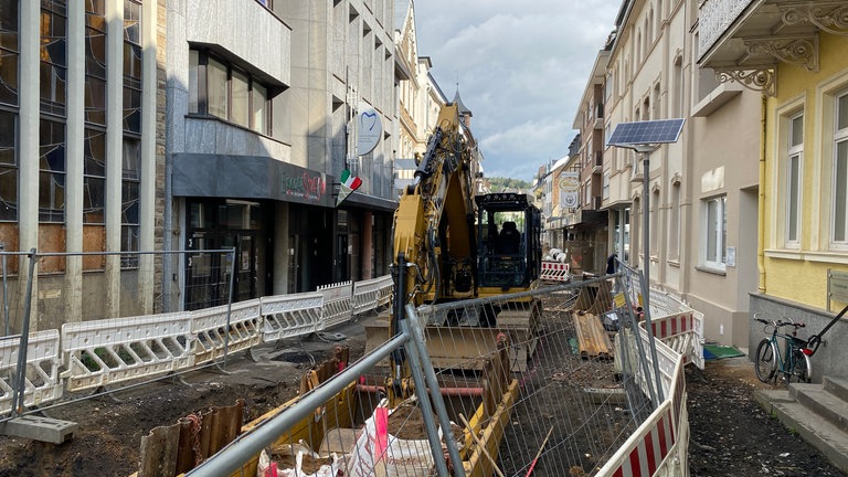 Ein Bagger hat mitten auf der von der Flut zerstörten Poststraße in Bad Neuenahr ein tiefes Loch gebaggert. Schon seit Monaten wird die Straße wieder hergerichtet. Anwohner sind Lärm und Schmutz ausgesetzt.