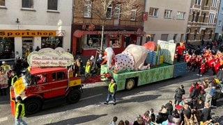 Ein Motivwagen beim Koblenzer Rosenmontagszug 2023: Ein deutscher Michel, dazu ein Schild mit der Aufschrift "Erbsen, Linsen, Kohl und Gras - Michel macht darauf Biosgas!"