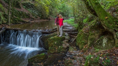 Ein Paar steht an einem kleinen Wasserfall an der Traumschleife Baybachklamm im Hunsrück.