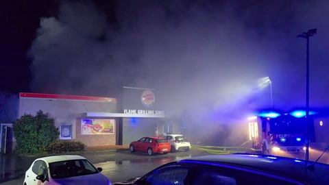 Die Burger King-Filiale in Lautzenhausen im Hunsrück brennt. Die Feuerwehr ist im Einsatz und löscht. Aus dem Gebäude schlagen Flammen und dichter Rauch.