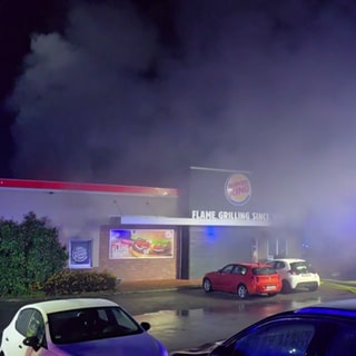 Die Burger King-Filiale in Lautzenhausen im Hunsrück brennt. Die Feuerwehr ist im Einsatz und löscht. Aus dem Gebäude schlagen Flammen und dichter Rauch.