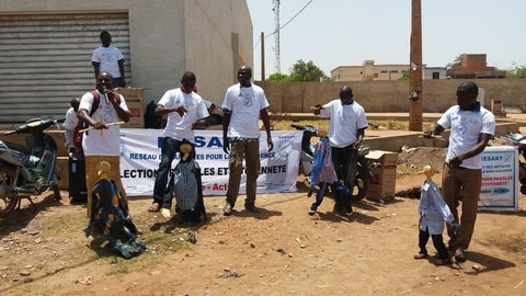 Mehrere Menschen stehen auf einer Straße in Mali und spielen mit Marionettenfiguren