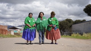 Drei Frauen in traditioneller Kleidung stehen auf einer Straße in Bolivien