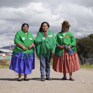 Drei Frauen in traditioneller Kleidung stehen auf einer Straße in Bolivien