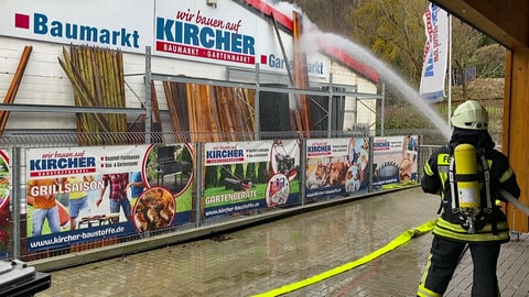 Feuerwehrleute halten einen starken Wasserstrahl auf den Baumarkt in Adenau, in dem ein Großbrand ausgebrochen ist.