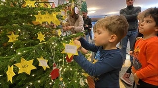 Kinder hängen Wunschsterne von Hilfsbedürftigen an den Caritas-Wunschbaum.