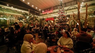 Menschen sitzen in einem Café mit einem Weihnachtsbaum und Weihnachtsschmuck in Damaskus.