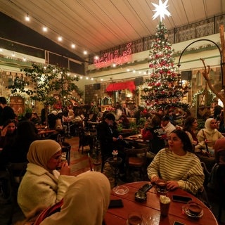 Menschen sitzen in einem Café mit einem Weihnachtsbaum und Weihnachtsschmuck in Damaskus.