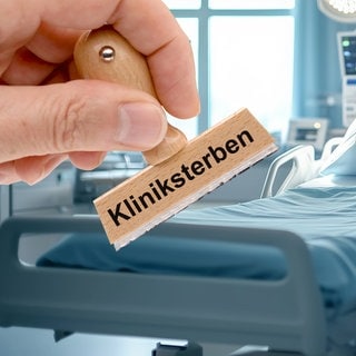 Kliniksterben - Ein Holzstempel ist beschriftet mit dem Aufdruck Kliniksterben über dem Bild von einem Krankenzimmer mit Bett in einem Krankenhaus - FOTOMONTAGE 