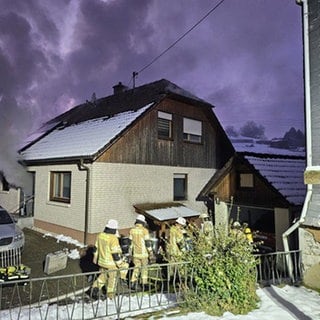 Feuerwehrleute stehen vor einem Haus, aus dem Rauch dringt.