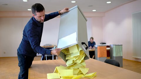 Ein Wahlhelfer leert gelbe Stimmzettel aus einer Wahlurne