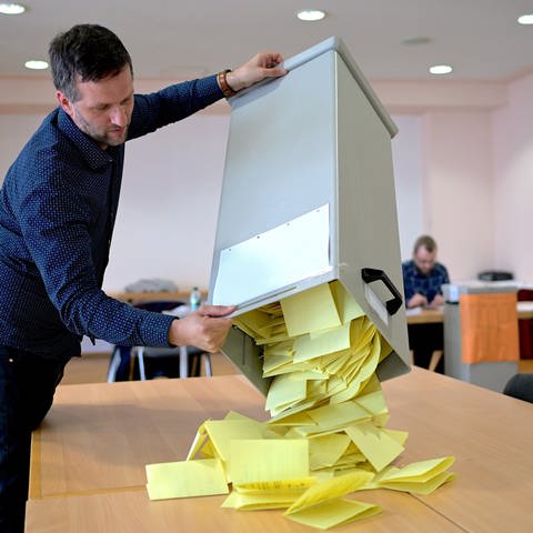 Ein Wahlhelfer leert gelbe Stimmzettel aus einer Wahlurne