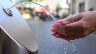 Eine Frau sammelt Wasser aus einem Trinkbrunnen in ihren Hände