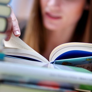 Frau liest ein Buch und sitzt zwischen einem Bücherstapel.