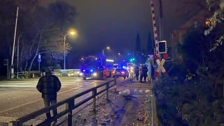 Ein Feuerwehrauto und ein Polizeiauto stehen im Dunkeln mit Blaulicht an dem Bahnübergang in Landau, wo eine Regionalbahn zuvor ein Auto erfasst hatte.
