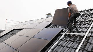 Solaranlagen sind auf Neubauten in Neustadt an der Weinstraße künftig Pflicht - Bild von einem Handwerker, der ein Solarpanel auf einem Dach montiert