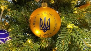 An einem geschmückten Baum in einem Geschäft hängt eine Kugel in den ukrainischen Nationalfarben Blau und Gelb mit dem Dreizack als Wappen.