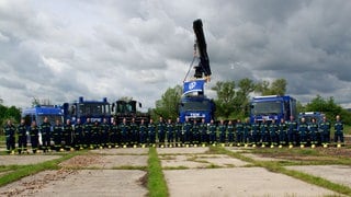 THW-Mitglieder stehen in dunkelblauen  Uniformen vor mehreren marineblauen Einsatzfahrzeugen, darunter einem Kran