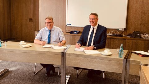 Landrat Clemens Körner (li.) und Minister Alexander Schweitzer unterzeichnen in Ludwigshafen im Verwaltungsgebäudes des Rhein-Pfalz-Kreises eine Vereinbarung zu IT-Sicherheit