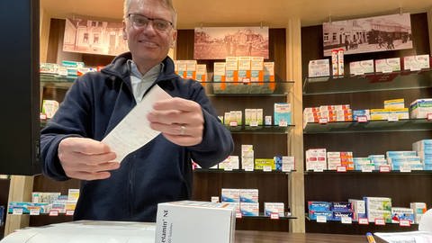 Apotheker Markus Wollny aus Ludwigshafen hält einen Kassenzettel in die Kamera in seiner Apotheke