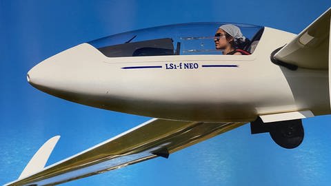 Mandelblütenkönigin Erva Satun fliegt mit Sonnenbrille als Pilotin ein Segelflugzeug vor blauem Himmel.