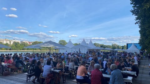 Am Rhein in Ludwigshafen stehen viele Bierzeltgarnituren. Daran sitzen sehr viele Menschen. Sie sind zum Eröffnungsabend des Festivals des deutschen Films gekommen.