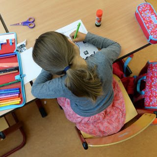 Schülerin sitzt über ihren Aufgaben in einer Schule: Symbolbild für Ludwigshafen muss seine Grundschulen für den Ganztagsbetrieb ausbauen 