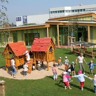 Kindertagesstättengebäude mit Kindern und Erzieherin - Symbolbild für Kreise müssen mehr für Kindergarten-Gebäude bezahlen