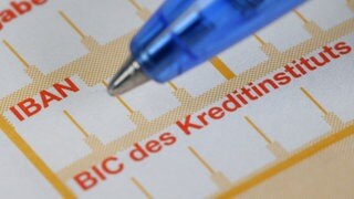 Ein Kugelschreiber ist neben einem Überweisungsträger mit den Schriftzügen "IBAN" und "BIC" zu sehen,