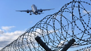 Ein Flugzeug hebt über einem Stacheldrahtzaun ab - Symbolbild: Ein straffälliger Somalier aus dem Kreis Südliche Weinstraße ist nach jahrelangem Hin und Her abgeschoben worden.