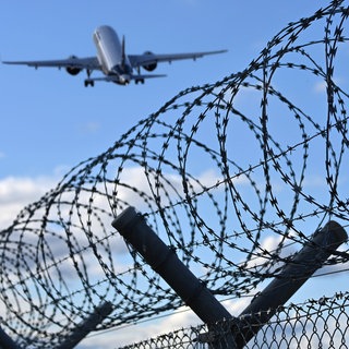 Ein Flugzeug hebt über einem Stacheldrahtzaun ab - Symbolbild: Ein straffälliger Somalier aus dem Kreis Südliche Weinstraße ist nach jahrelangem Hin und Her abgeschoben worden.