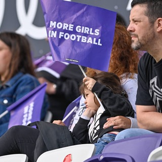 Ein Mädchen hält eine Fahne hoch mit der englischen Aufschrift: "Mehr Frauen im Fußball" - In Ludwigshafen haben Mädchen gelernt, junge Fußballerinnen zu trainieren.