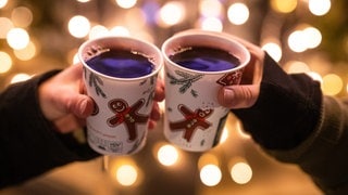 Zwei Frauen stoßen mit Glühwein in Bechern auf dem Weihnachtsmarkt an.