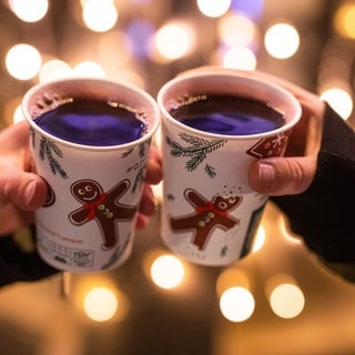 Zwei Frauen stoßen mit Glühwein in Bechern auf dem Weihnachtsmarkt an.