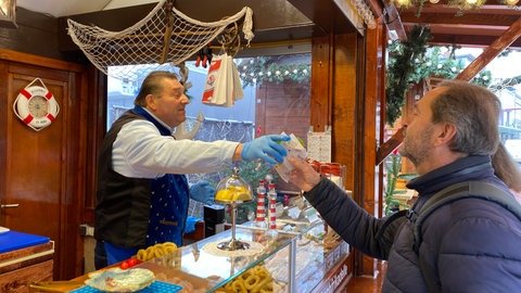 Buden auf Weihnachtsmarkt Ludwigshafen 2024. Einer der ersten Besucher kauft sich Calamaris an Fiischbude. 