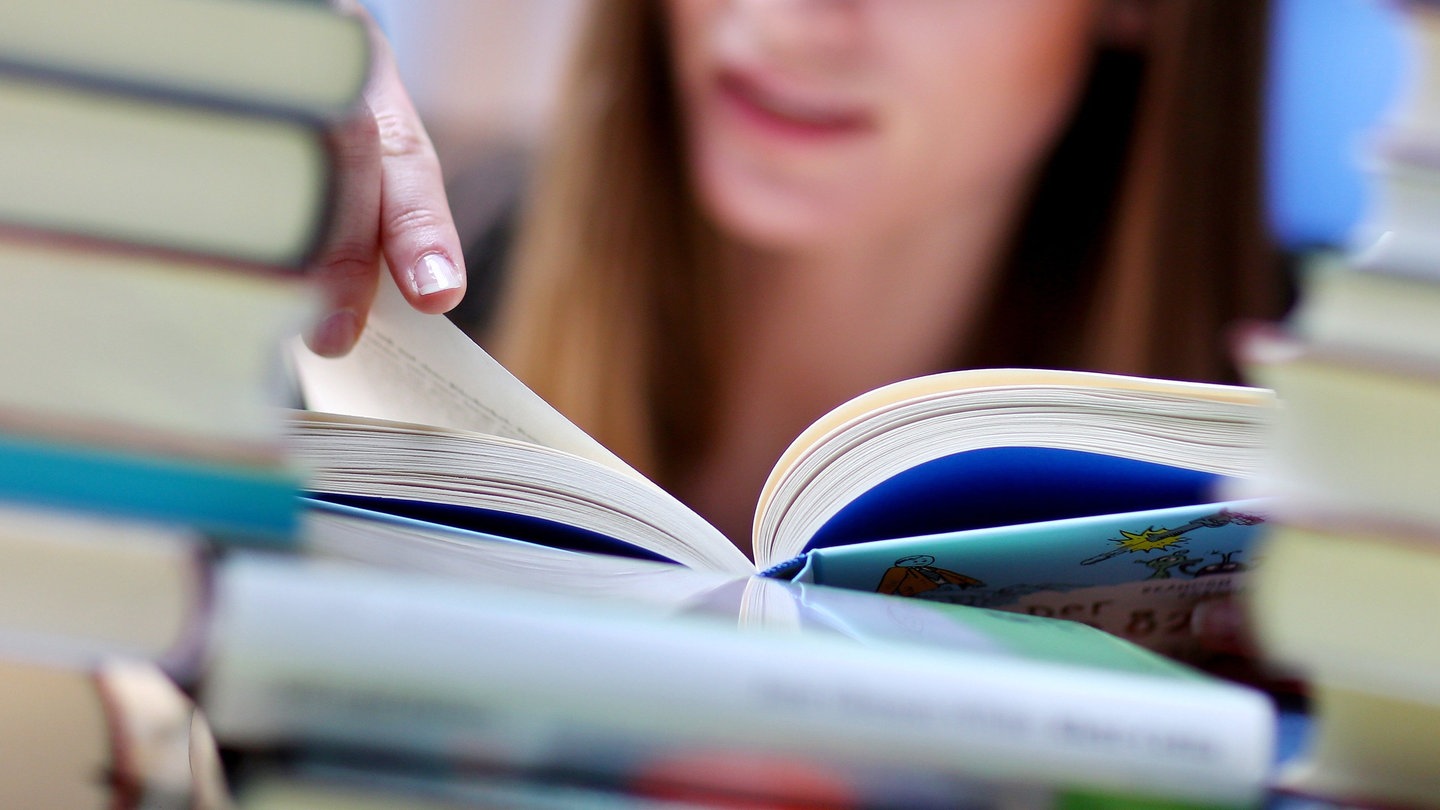 Frau liest ein Buch und sitzt zwischen einem Bücherstapel.