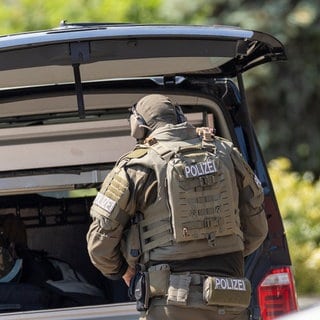 Ein Mitglied des SEK steht mit Schutzausrüstung und dem Rücken zur Kamera vor einem geöffneten Kofferraum. In Annweiler am Trifels kam es jetzt auch zu einem SEK-Einsatz, weil ein Mann mit einer Schusswaffe hantierte.