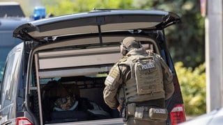 (Symbolbild) Ein Mitglied des SEK steht mit Schutzausrüstung und dem Rücken zur Kamera vor einem geöffneten Kofferraum. In Annweiler am Trifels kam es jetzt auch zu einem SEK-Einsatz, weil ein Mann mit einer Schusswaffe hantierte.