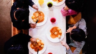 Kinder essen an Tisch mit bunten Bechern (Symbolbild). Die Aktion Kindervesperkirche wird dieses Jahr in Ludwigshafen auf zwei Wochen verlängert.